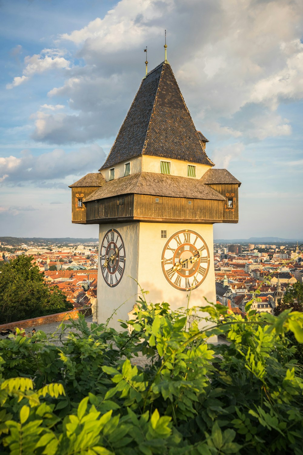 a clock tower with a weather vane with Graz in the background