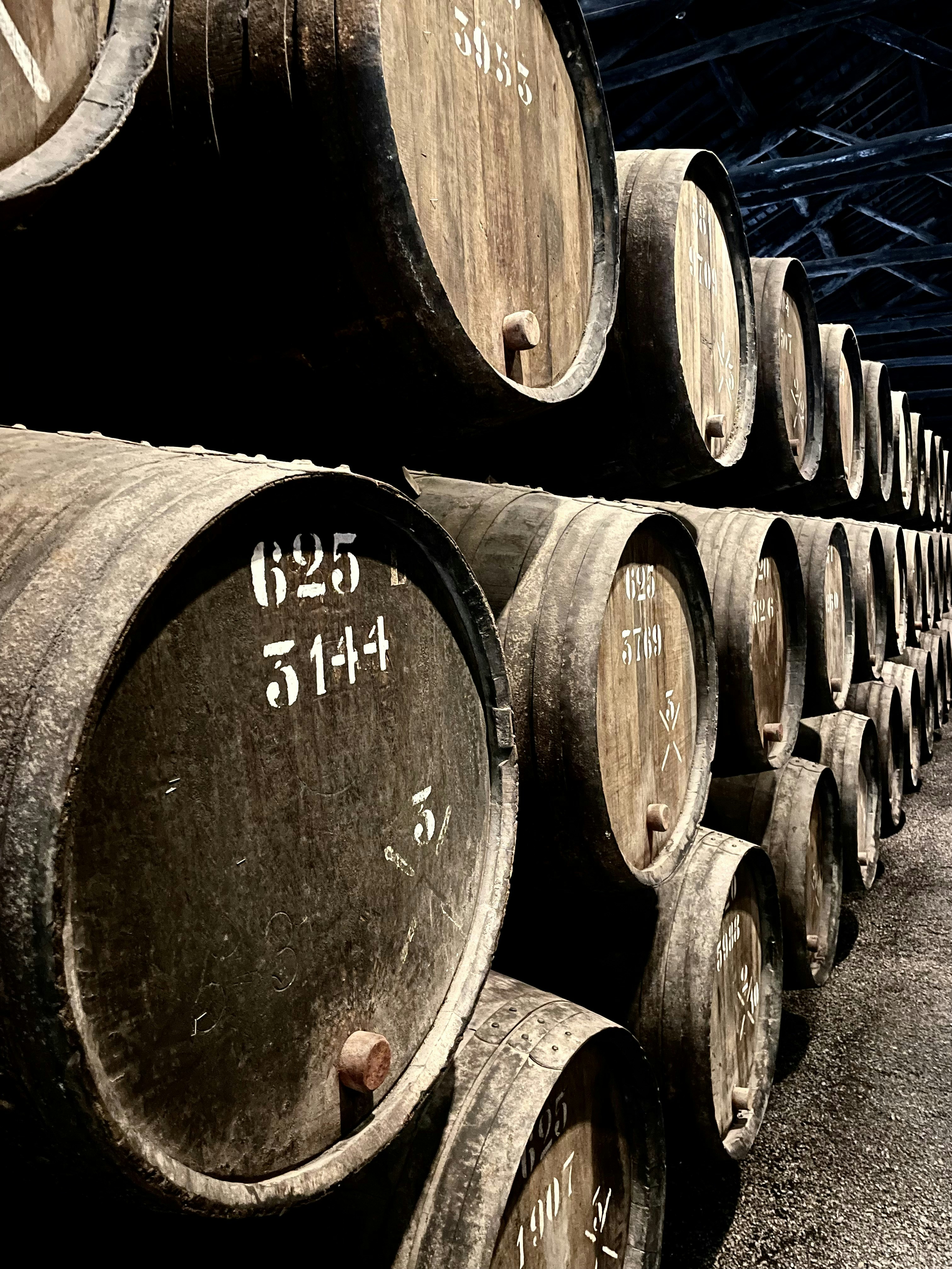 Oak barrels in stone cellar, dim candlelight, deep shadows, aged wooden casks in rows