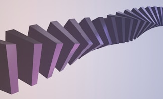 A series of three-dimensional dark purple blocks are arranged in a curved, cascading pattern, creating an optical illusion. The background transitions from a light cream to a soft blue, enhancing the abstract and surreal effect of the composition.