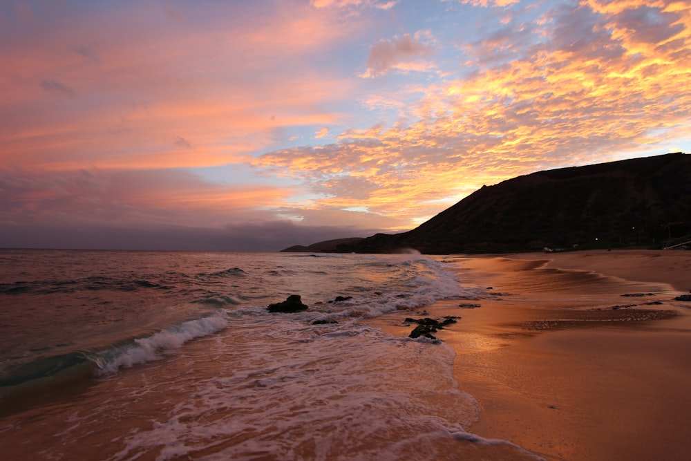 a beach with waves and a hill in the background