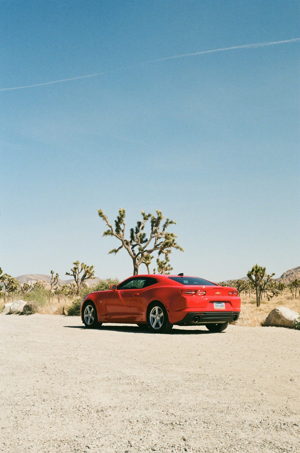 a red car parked on a dirt road with a tree and blue sky
