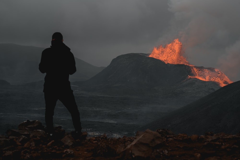 a man standing on a rocky shore looking at a volcano
