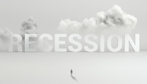 Large letters spelling 'RECESSION' are positioned above a flat, fog-covered landscape. A solitary figure stands below the letters, dwarfed by their size. Billowing clouds of smoke or fog provide a dramatic backdrop, accentuating the sense of isolation.