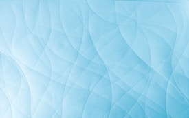 A textured surface with intricate overlapping patterns creating a series of flowing, curved lines. The design is uniform and features a soft blue hue.