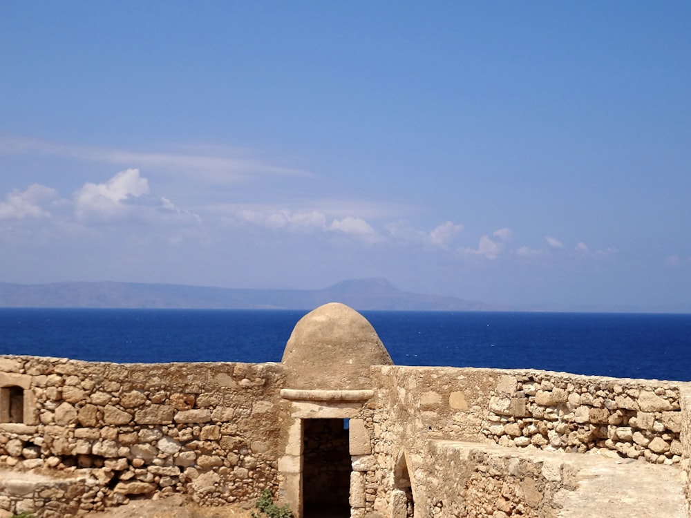 a stone wall with a stone wall and a body of water in the background