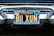 A vintage California license plate with the number 811 XUN is mounted on a classic car. The frame around the license plate is metallic, and the plate displays registration information, including 'Vallejo' and 'Earl A. Jensen'. The chrome bumper and grille of the car are visible, reflecting light and emphasizing the antique style.