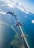 Three skydivers are freefalling above a coastal landscape with clear blue skies and scattered clouds. The ocean and shoreline are visible below, creating a breathtaking view from high altitude.