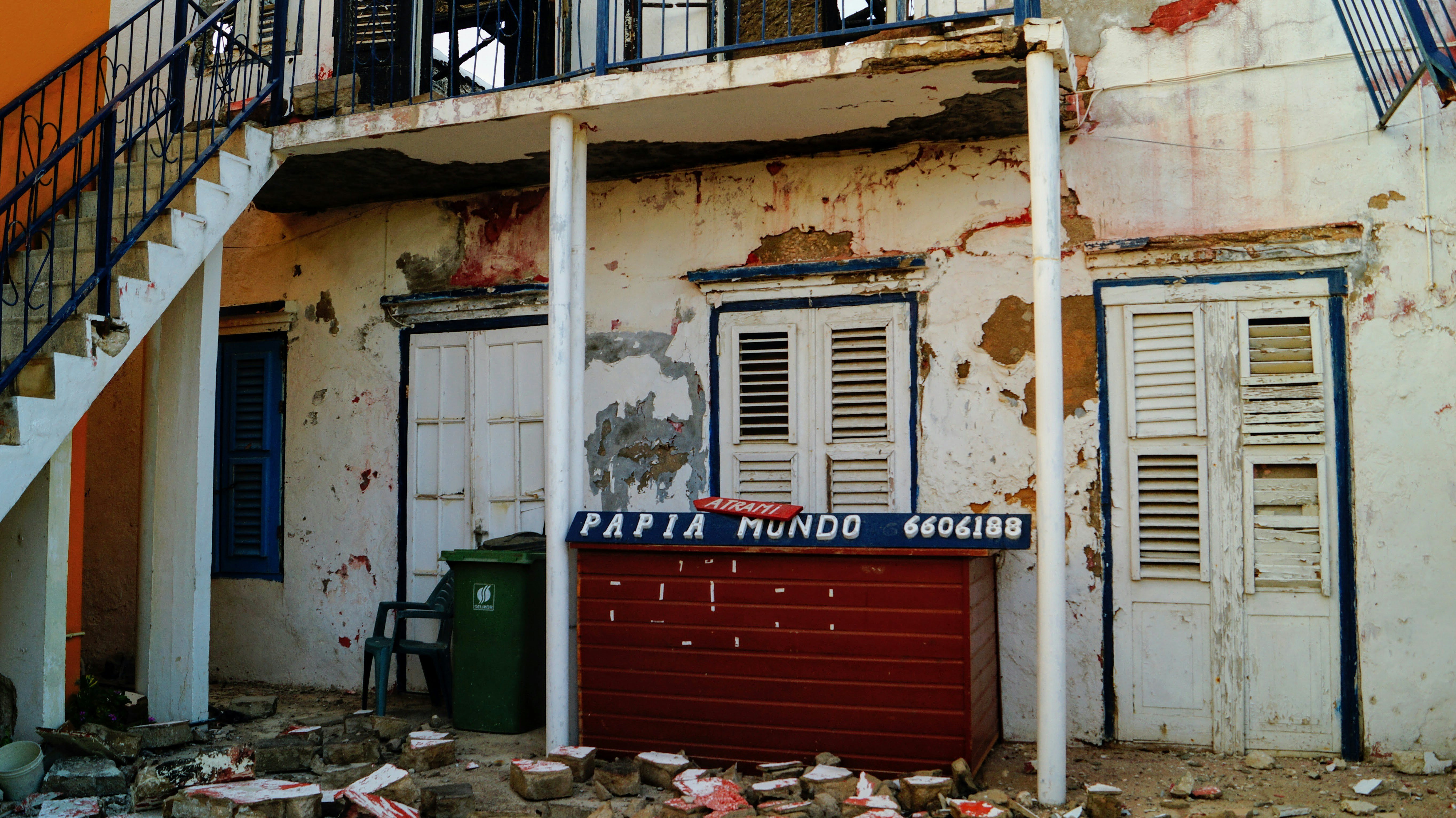 a building with a red door and a green trash can in front