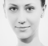 A black and white close-up portrait of a person with a calm expression, displaying symmetrical facial features and smooth skin. The photo emphasizes the eyes and the subtle curve of the lips.