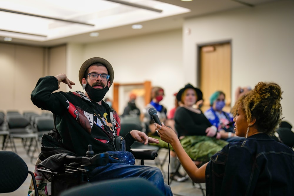 a person sitting in a chair with a microphone in front of a group of people