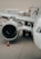 A close-up view of an airplane on a tarmac, focusing on the engine and wing. A cargo container marked ANA Cargo is in the background with two workers nearby. An orange safety cone is placed near the engine.