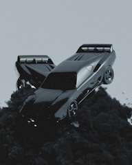 A sleek, futuristic car seems to be floating or emerging from dark, billowing smoke against a muted gray background. The car has a shiny, reflective surface and aerodynamic design, emphasizing speed and modernity.