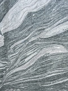 A close-up view of a textured stone surface with swirling patterns of white and grey. The natural design resembles waves or flowing lines, providing an abstract and intricate appearance.