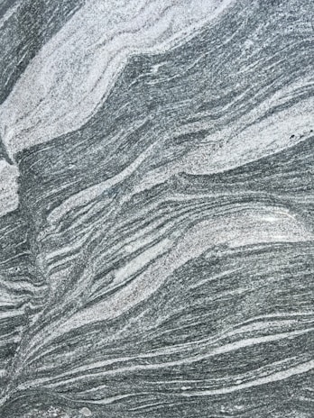A close-up view of a textured stone surface with swirling patterns of white and grey. The natural design resembles waves or flowing lines, providing an abstract and intricate appearance.
