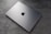 A sleek, silver laptop with a prominent logo on top is resting on a textured, grey surface. The laptop appears closed and is positioned at an angle that highlights its thin design.