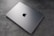A sleek, silver laptop with a prominent logo on top is resting on a textured, grey surface. The laptop appears closed and is positioned at an angle that highlights its thin design.