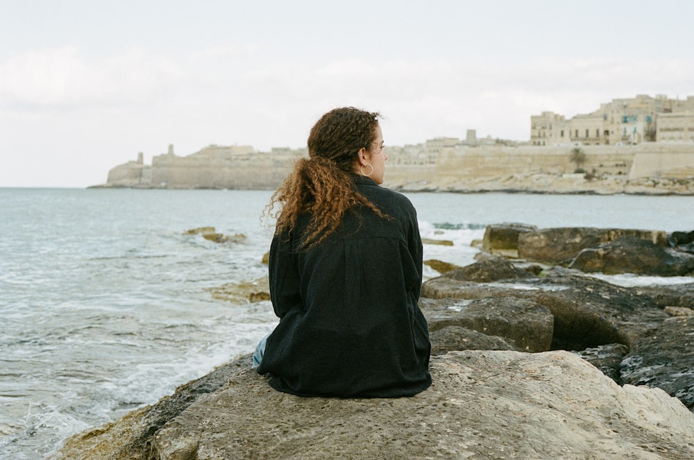 a person sitting on a rock by the water