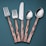 A set of cutlery consisting of two forks, a knife, and two spoons arranged vertically on a teal background. The handles have a copper tone with a textured, faceted design, while the fork and spoon heads, including the knife blade, are polished, reflecting light.