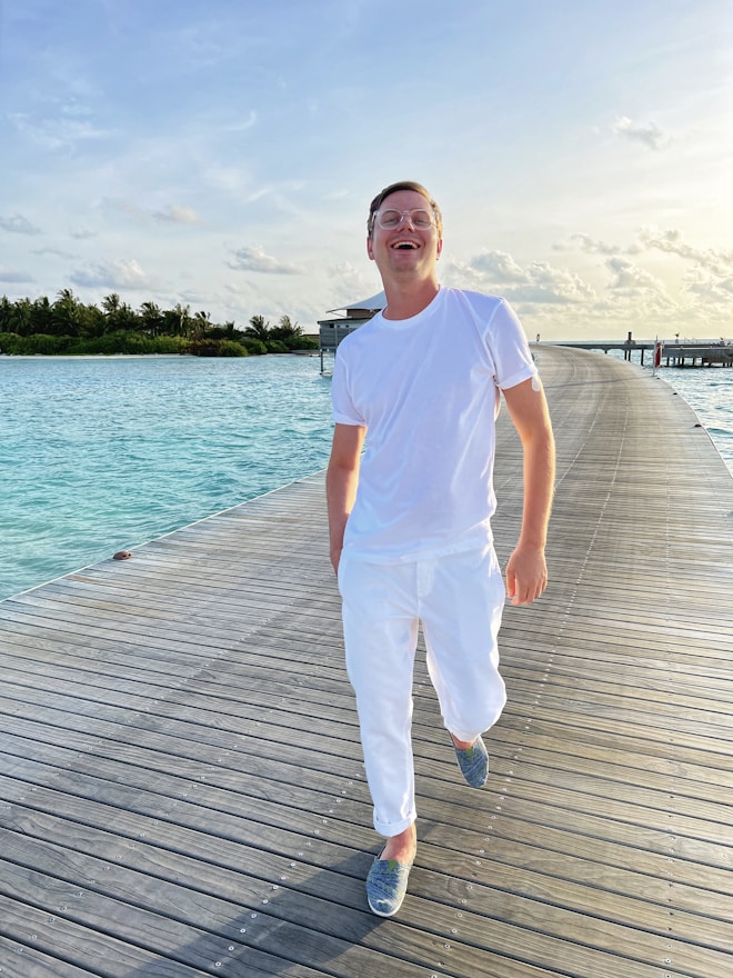 a man wearing white t-shirt and white pants is standing on a dock