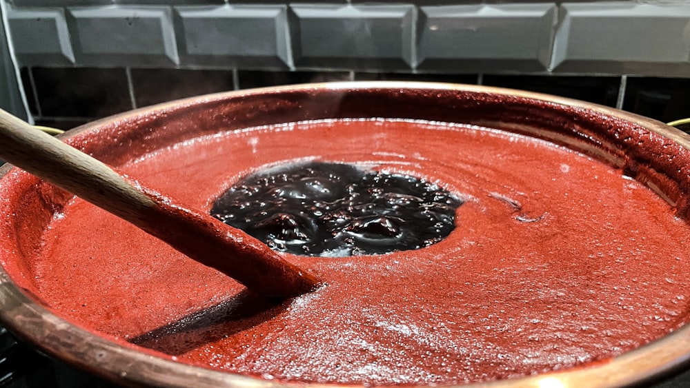 a wooden spoon in a bowl of red liquid