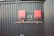Two red electrical devices are mounted on a black corrugated metal wall, connected by a series of cables. The setup includes several black wires attached to the devices and a metal rack supporting the components.