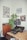A room corner features a wooden cabinet topped with a turntable and a speaker. A large speaker with two smaller electronic devices and a yellow cable lies on a wooden desk. A leafy plant and wall art including posters and an album cover add character to the space.