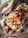 A homemade cake topped with cream frosting, pecans, and fresh strawberries, placed on a checkered cloth with additional strawberries and pecans scattered around.