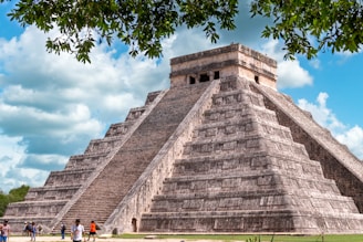a large pyramid with people standing around with Chichen Itza in the background