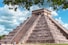 a large pyramid with people standing around with Chichen Itza in the background