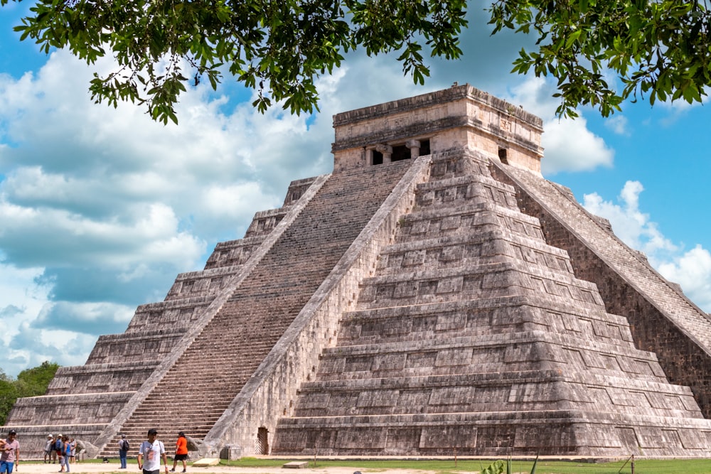 a large pyramid with people standing around with Chichen Itza in the background