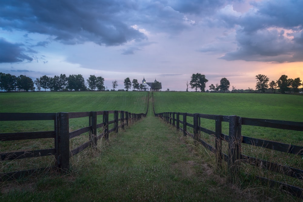 a fenced in field with a wooden gate and a house in the distance