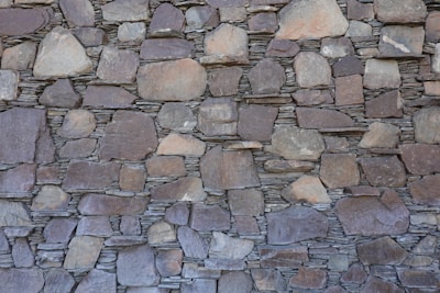 A wall constructed of irregularly shaped, stacked stone slabs with a mix of earthy tones and textures. The stones vary in size, from large flat pieces to smaller ones, and are meticulously arranged to fit together tightly.