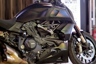 A sleek, modern motorcycle with a matte black finish is prominently displayed. The close-up view highlights the intricate details of its engine and bodywork, showcasing the brand logo on the engine cover. The vehicle's design features sharp lines and polished metallic elements, with dual exhaust pipes visible at the bottom.