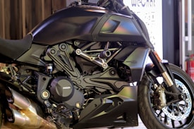 A sleek, modern motorcycle with a matte black finish is prominently displayed. The close-up view highlights the intricate details of its engine and bodywork, showcasing the brand logo on the engine cover. The vehicle's design features sharp lines and polished metallic elements, with dual exhaust pipes visible at the bottom.