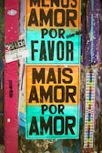A wall covered with colorful graffiti and posters. Two prominent posters with large black text on multicolored backgrounds. One reads 'Menos Amor Por Favor' and the other 'Mais Amor Por Amor'. The wall also has various other small stickers and graffiti in different colors, mainly purple and teal.