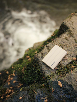 A sleek, compact outdoor power bank resting on a rugged rock beside a flowing mountain stream.