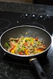 Shiny stainless steel frying pan reflecting the kitchen lights, filled with a colorful stir-fry