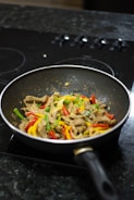 Shiny stainless steel frying pan reflecting the kitchen lights, filled with a colorful stir-fry
