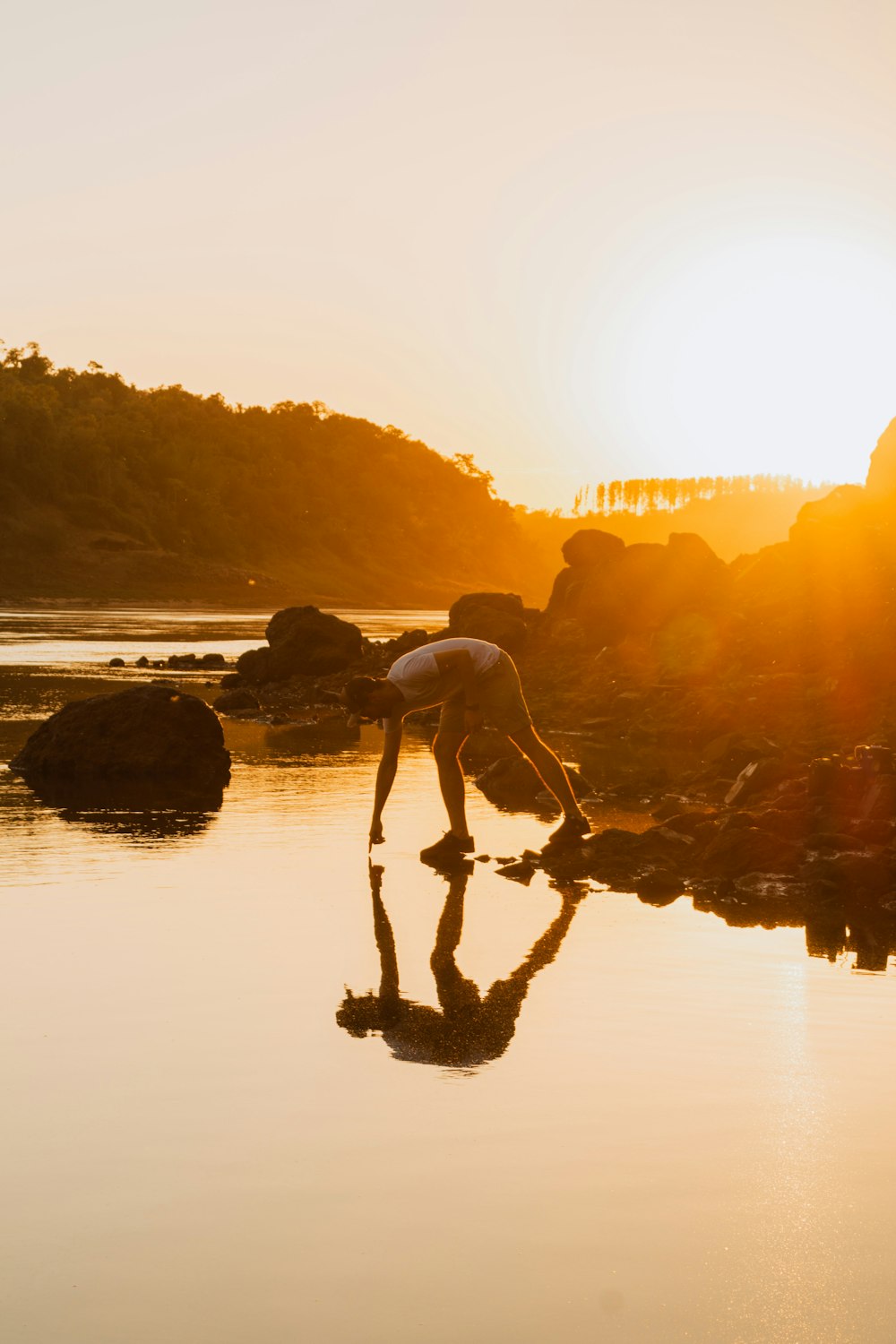 a person bending over to touch a rock in the water