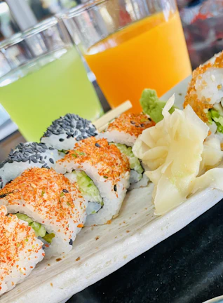 Close-up of a colorful sushi roll topped with fresh ginger and sesame seeds on a rustic wooden board.