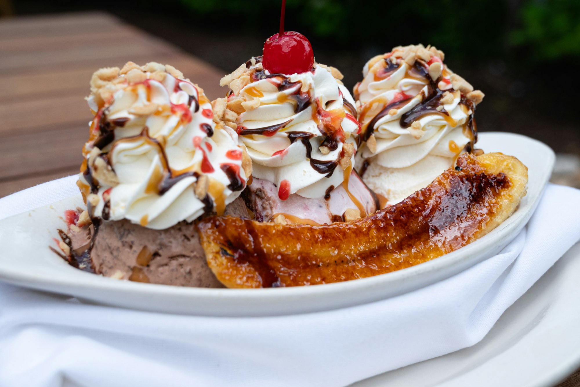 Banana Split with bruleed banana, three scoops of ice cream, whipped cream, and cherry on top.