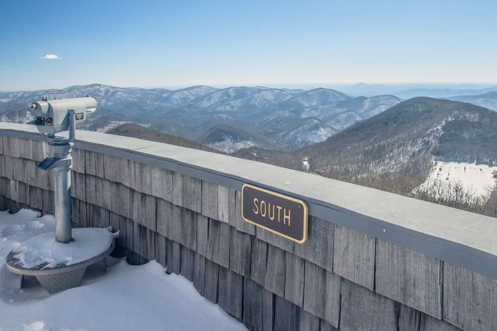 a wooden fence with a sign on it and mountains in the background