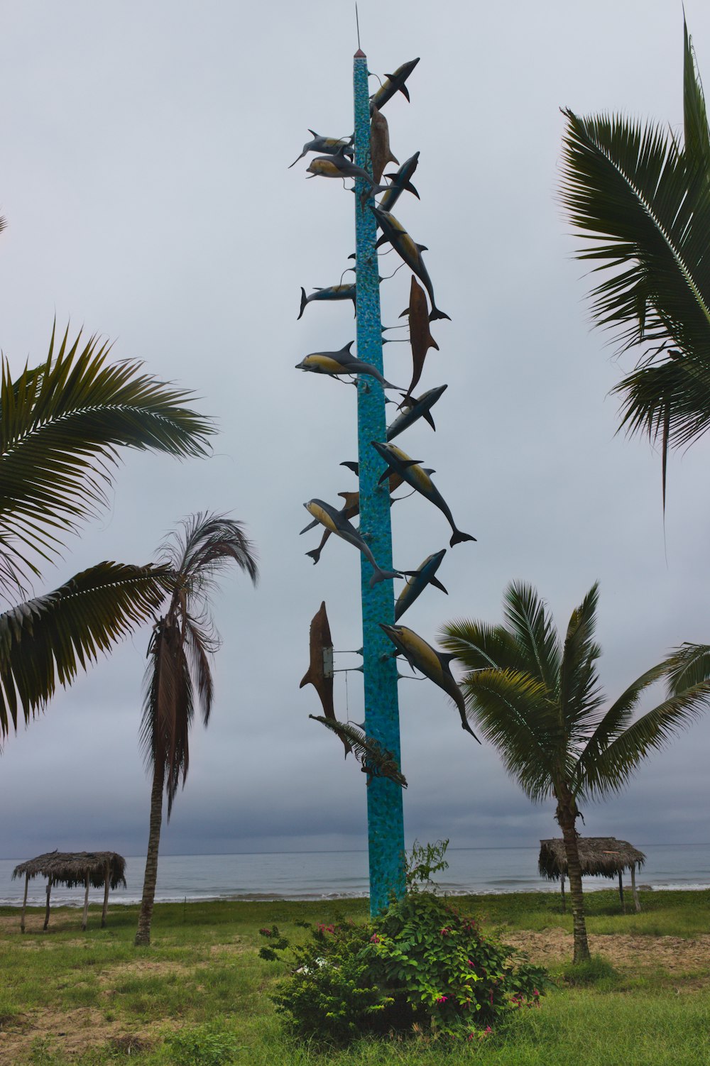 a tall pole with a bird on it by palm trees and a body of water