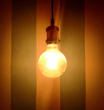 A bright light bulb glowing warmly against a backdrop of the Colombian flag colors.
