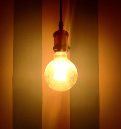 A bright light bulb glowing warmly against a backdrop of the Colombian flag colors.