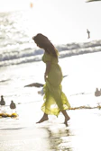 Woman walking along the beach in a breezy floral dress, sunlight sparkling on the water.