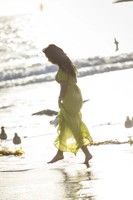 Woman walking along the beach in a breezy floral dress, sunlight sparkling on the water.