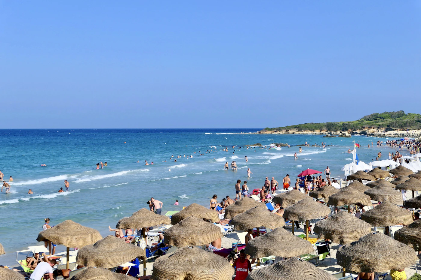 A packed Mediterranean beach lined edge to edge with umbrellas in peak August — the crowd level September travelers are trying to avoid