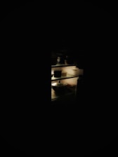 A dimly lit refrigerator interior containing several containers and a pot. The fridge's light creates a stark contrast between the illuminated shelves and the surrounding darkness.