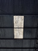 A corrugated metal roof with a rectangular section that is translucent or a different color, allowing light to pass through. The roof structure includes multiple lines and patterns in its design, with some areas appearing worn or weathered.